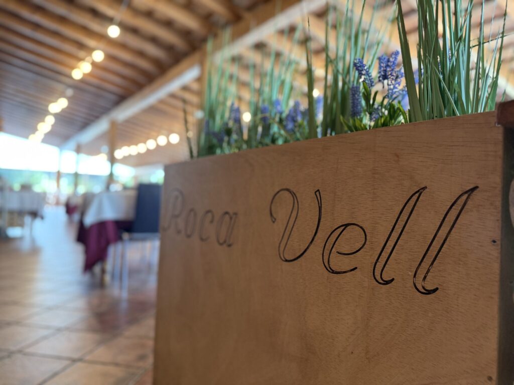 Cartel de madera tallado con el nombre Masia Roca Vell en la terraza del restaurante en Lliçà d'Amunt