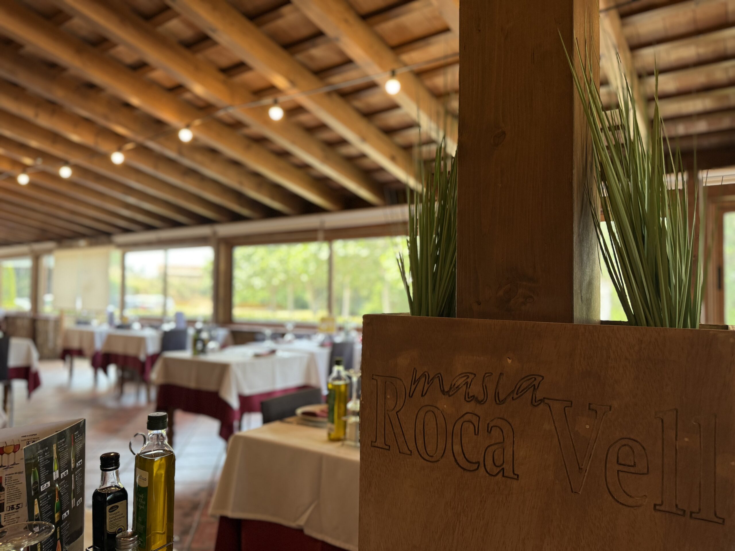 Comedor interior de Masia Roca Vell con techo de vigas de madera y grandes ventanales