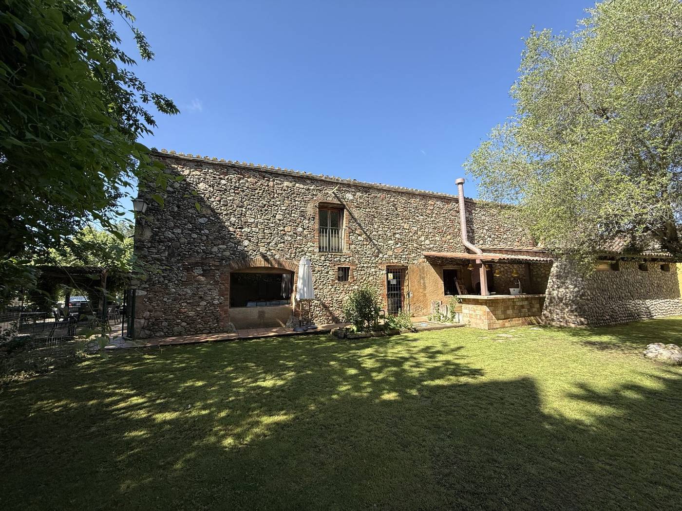 Fachada de piedra de Masia Roca Vell con jardín de césped en Lliçà d'Amunt